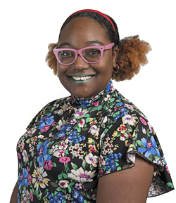 isana skeete wearing a colourful flowery top and smiling wearing pink glasses and green lipstick